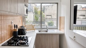 A modern kitchen with a gas stove, wooden cabinets, a sink, and a view of the city through a large window. - Blueground | Auteuil, balcony, nr Parc de Princes (Paris)