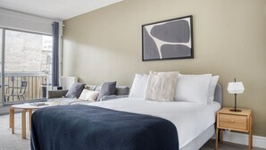 A hotel room with a bed, bedside table, lamp, and a view of the outside balcony. - Blueground | Auteuil, balcony, nr Parc de Princes (Paris)