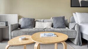 A modern living room with a grey sofa, two wooden side tables, and a framed abstract art piece on the wall. - Blueground | Auteuil, balcony, nr Parc de Princes (Paris)