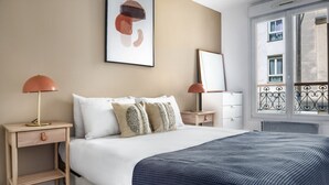A bedroom with a bed, two bedside tables, a nightstand, a window with a view, and a painting on the wall. - Blueground | Sentier, furnished, nr Montorgueil St (Paris)