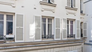 Une façade d’immeuble dotée de nombreuses fenêtres et volets, d’un socle en pierre et d’un balcon avec des garde-corps en métal.