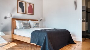 Un dormitorio moderno con una cama de madera, sábanas blancas, almohadas estampadas y una manta azul oscuro.