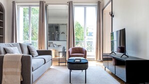 Una sala moderna con un sofá gris, una mesita redonda pequeña, un sillón rojo y un televisor sobre un mueble.