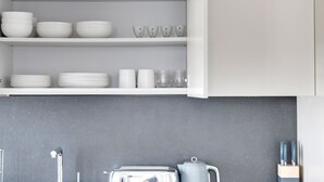 A kitchen with white cabinets, a grey countertop, and various kitchenware including bowls, plates, and glasses.