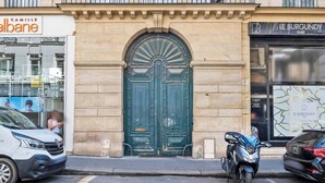 A street view with a green double door, a white car, and a motorcycle parked on the sidewalk.
