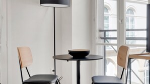 A modern interior with a round table, two chairs, a black floor lamp, and a window with a view of buildings.