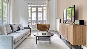 Un salon moderne avec un canapé gris, une table basse ronde, un meuble en bois et un téléviseur fixé au mur.