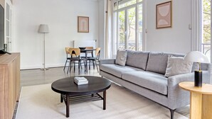 Un salon moderne avec un canapé gris, une table basse ronde, une table à manger avec des chaises et un lampadaire.