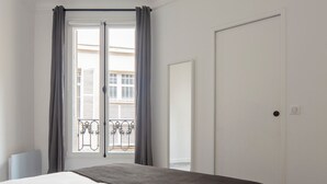 Une chambre à coucher avec un lit, une fenêtre avec des rideaux, une porte et une vue sur un balcon doté de balustrades.