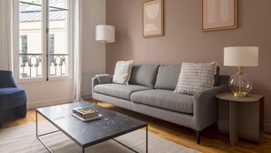Un salon avec un canapé gris, deux lampes, une table basse et un fauteuil bleu.