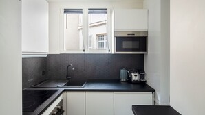Une cuisine compacte dotée d’un plan de travail noir, d’un évier en acier inoxydable, d’un four à micro-ondes encastré et d’une cuisinière à gaz.