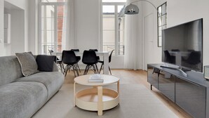 A modern living room with a grey sofa, a round coffee table, a TV, and a dining area with chairs and a table. - Blueground | Sentier, balcony, nr Les Halles (Paris)