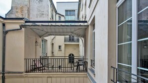 A narrow courtyard with a covered outdoor seating area, a small table, and chairs. - Blueground | Sentier, balcony, nr Les Halles (Paris)