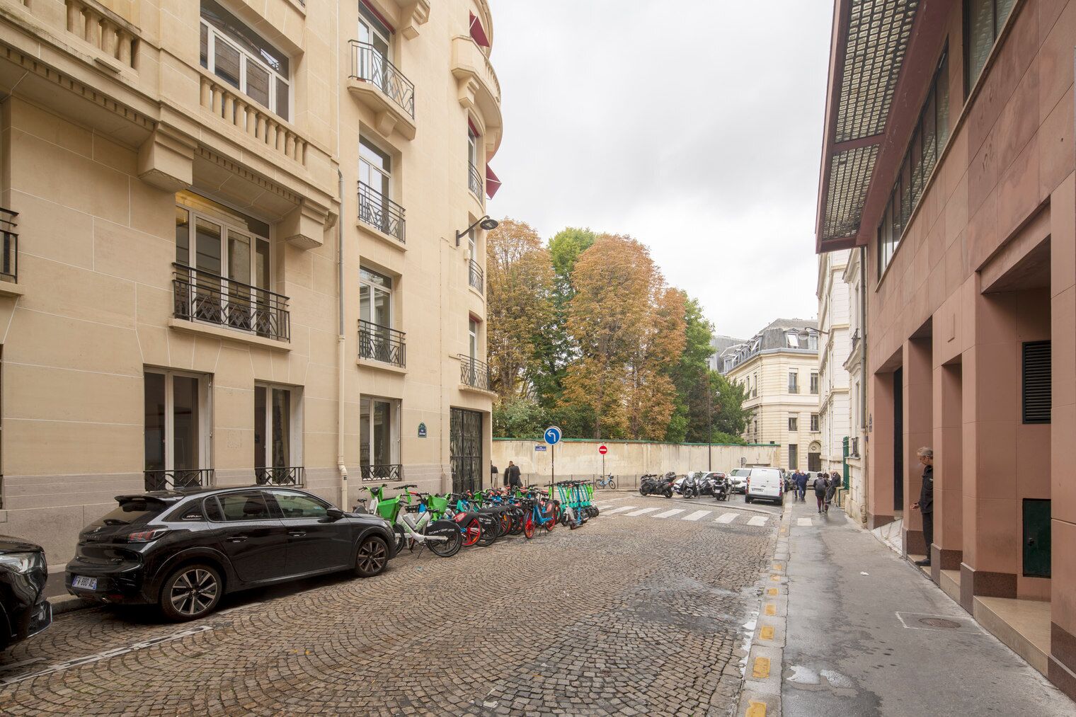 A cobblestone street lined with buildings, a parked car, and a row of bicycles.