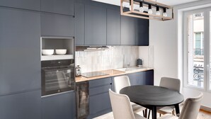 A modern kitchen with dark blue cabinets, a built-in oven, and a dining area with a round table and chairs.