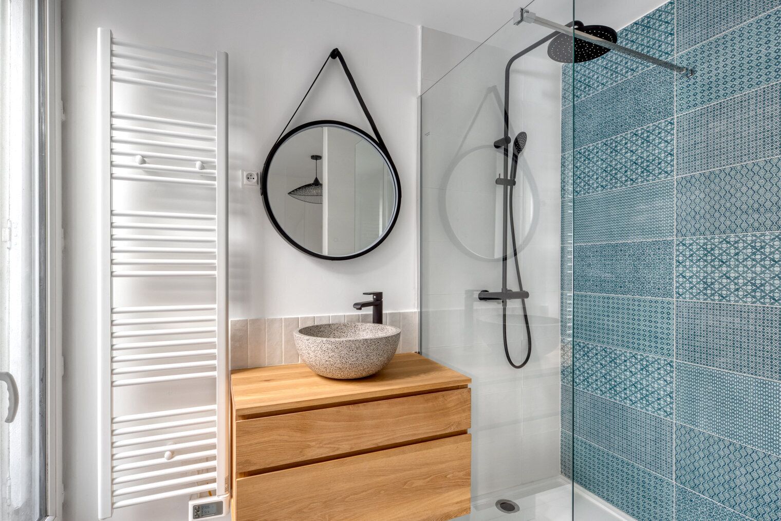 A modern bathroom with a round mirror, a vessel sink, a handheld showerhead, and a glass-enclosed shower.