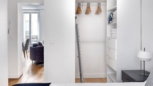 A bedroom with a bed, a nightstand, a lamp, and a closet with hanging clothes and a shelf.
