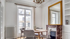 A room with a round table, four chairs, a fireplace, a large mirror, and a radiator. - Blueground | Le Marais, elevator, nr Rue Rambuteau (Paris)