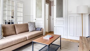 A living room with a beige sofa, a wooden coffee table, and a lamp. - Blueground | Le Marais, elevator, nr Rue Rambuteau (Paris)