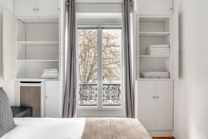 A bedroom with a bed, a wardrobe, and a balcony with a view of trees.