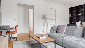 A modern living room with a grey sofa, a wooden coffee table, a desk with a chair, and a black bookshelf.