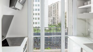 A modern kitchen with a built-in stove, white cabinetry, and a balcony with a view of a high-rise building. - Blueground | Bir Hakeim, nr Eiffel Tower (Paris)