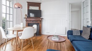 A living room with a fireplace, a television, a dining table with chairs, a sofa, and a coffee table. - Blueground | Bir Hakeim, nr Eiffel Tower (Paris)