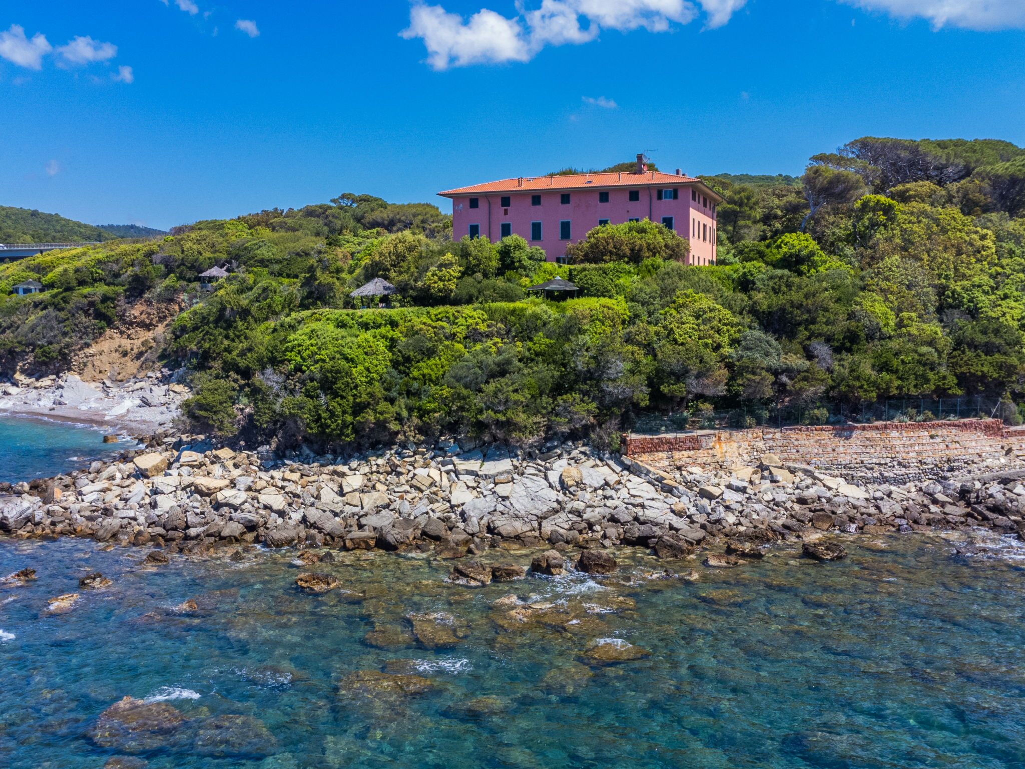 A coastal building surrounded by rocky terrain and clear blue waters.