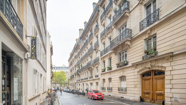Une rue étroite bordée de bâtiments historiques, où l’on aperçoit une voiture rouge garée sur le côté et une rangée de motos stationnées.