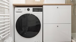 Une petite buanderie moderne, dotée d’un lave-linge à chargement frontal et d’un petit meuble de rangement.