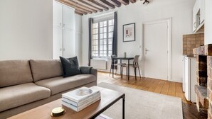 A modern living room with a sofa, a coffee table with books, a dining area with chairs, and a fireplace. - Blueground | Le Marais, nr Les Halles (Paris)