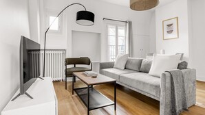 A modern living room with a sofa, a coffee table, a chair, a TV, and a lamp. - Blueground | Ecole Militaire, furnished, balcony (Paris)