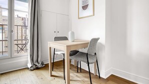 A modern dining area with a wooden table and two chairs, a white cabinet, and a framed artwork on the wall. - Blueground | Ecole Militaire, furnished, balcony (Paris)