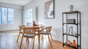 Ein Essbereich mit einem runden Holztisch und vier Stühlen, einem schwarzen Metallregal mit Dekoration und einem großen abstrakten Gemälde an der Wand.