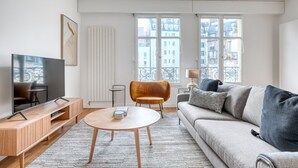 Ein modernes Wohnzimmer mit Flachbildfernseher, einer Couch, einem Couchtisch und einem Sessel.