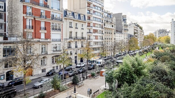 Una hilera de edificios de varios pisos con balcones, coches aparcados y árboles a lo largo de la calle.