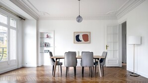 Comedor con suelo de madera en patrón de espiga, pared blanca con un cuadro abstracto enmarcado y una lámpara colgante moderna.