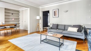 Uma sala de estar moderna com um sofá cinza, mesa de centro de madeira e um espaço de refeições com um banco e mesa.