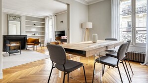 Uma sala de estar ampla com uma grande mesa de jantar de madeira, assentos confortáveis, lareira e vista para a cidade através de janelas grandes.