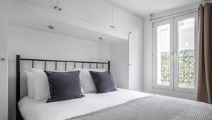 A bedroom with a bed, white walls, a window with curtains, and a view of greenery outside. - Blueground | Palais Royal, balcony, nr Louvre (Paris)