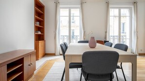 Un salon moderne doté d’une grande bibliothèque en bois, d’une table à manger avec des chaises et offrant une vue sur la ville grâce à de grandes fenêtres.