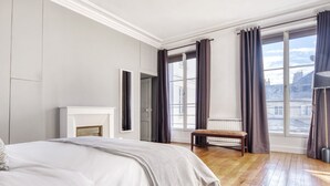 Ein Schlafzimmer mit einem großen Bett, einem Kamin, einer Bank und Blick auf die Stadt durch große Fenster.