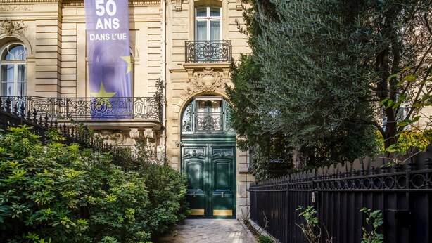 A historic building with a green double door, ornate iron railings, and a banner celebrating 50 years. - Blueground | Arc de Triomphe, nr Champs Elysées (Paris)