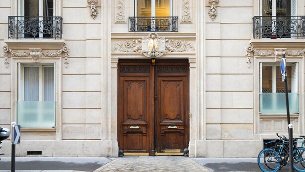 A building with a double wooden door, ornate window frames, and a metal balcony railing. - Blueground | Monceau, a/c, nr Parc Monceau (Paris)