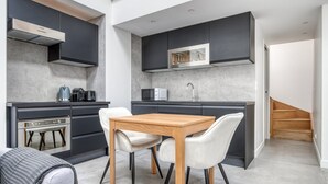 A modern kitchen with dark cabinetry, a wooden dining table, and a built-in microwave. - Blueground | Monceau, a/c, nr Parc Monceau (Paris)
