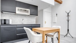 A modern kitchen with dark cabinetry, a microwave, and a wooden dining table with two chairs. - Blueground | Monceau, a/c, nr Parc Monceau (Paris)
