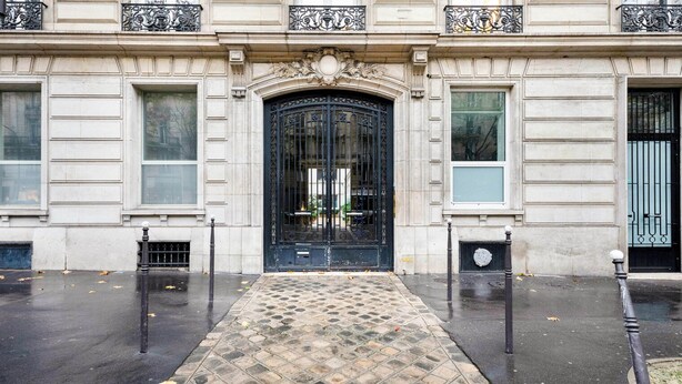 A building with a large black ornate entrance, a tiled pavement, and a stone facade. - Blueground | Miromesnil, furnished, elevator (Paris)