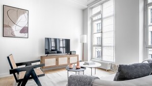 A modern living room with a flat-screen TV, a sofa, a coffee table, and a bookshelf.