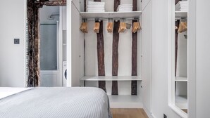 A bedroom with a bed, wooden beams, and built-in storage with hanging clothes and folded towels.