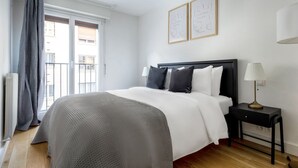 A hotel room with a large bed, a bedside table with a lamp, and two framed pictures on the wall. - Blueground | Porte de Champerret, elevator (Paris)